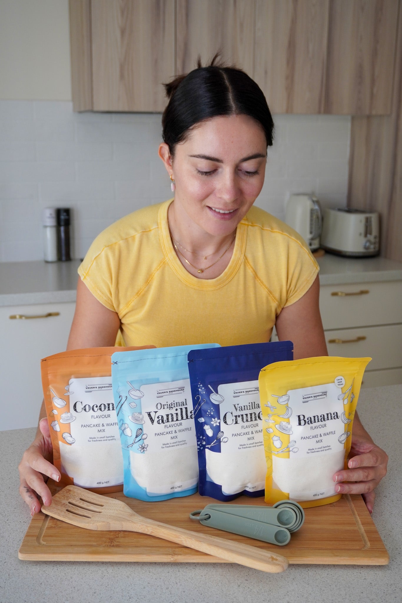 Woman holding packages of different flavored pancake mixes in a kitchen setting