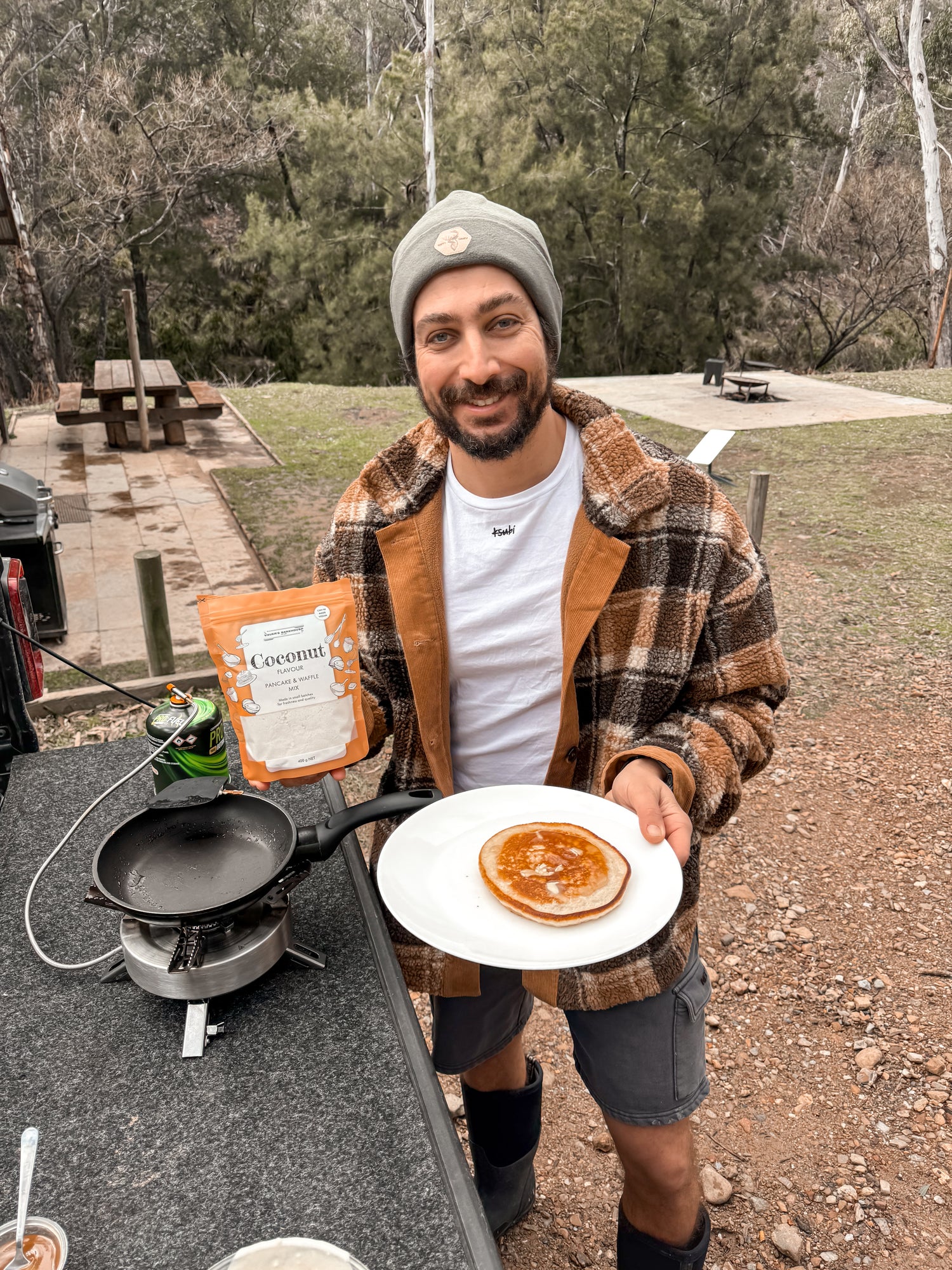 Man cooking pancakes outdoors at a campsite with a pan and a plate - Sauer's Bakehouse